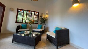 A room with two wicker sofas, a glass coffee table, a ceiling fan, and a wall-mounted light fixture. - Casa Pirata (Isla Holbox)