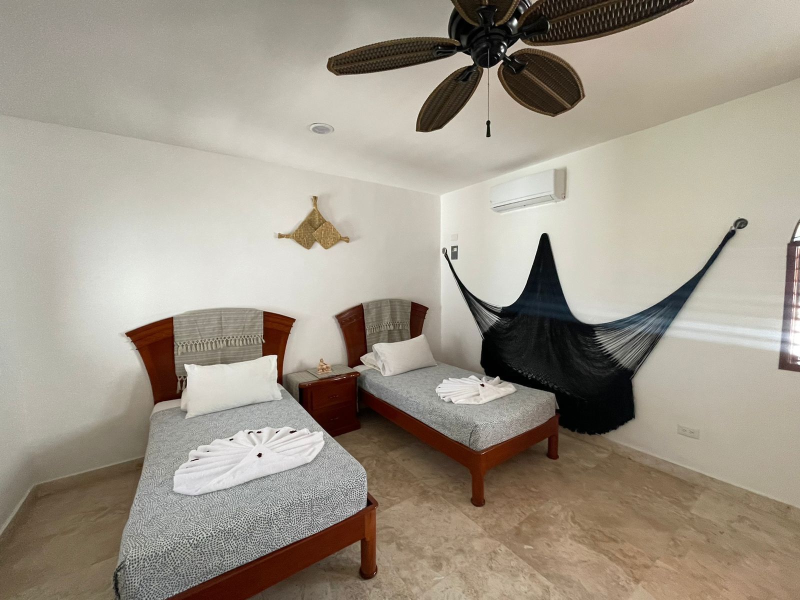 A room with two beds, a ceiling fan, a hammock, and a wall-mounted air conditioner.