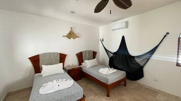 A room with two beds, a ceiling fan, a hammock, and a wall-mounted air conditioner.