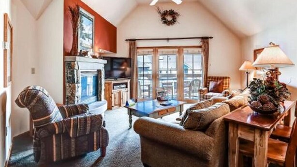 A cozy living room with a fireplace, a ceiling fan, and a large window. - River Run by Wyndham Vacation Rentals (Keystone)
