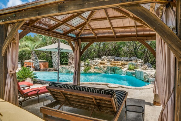 A covered outdoor area with a pool, lounge chairs, and a pergola structure. - Romantic Getaway Cottage with Hot Tub and Resort Amenities (Helotes)