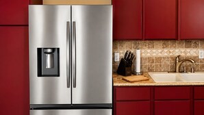 A stainless steel refrigerator with a water dispenser, a sink with a faucet, and a knife block.