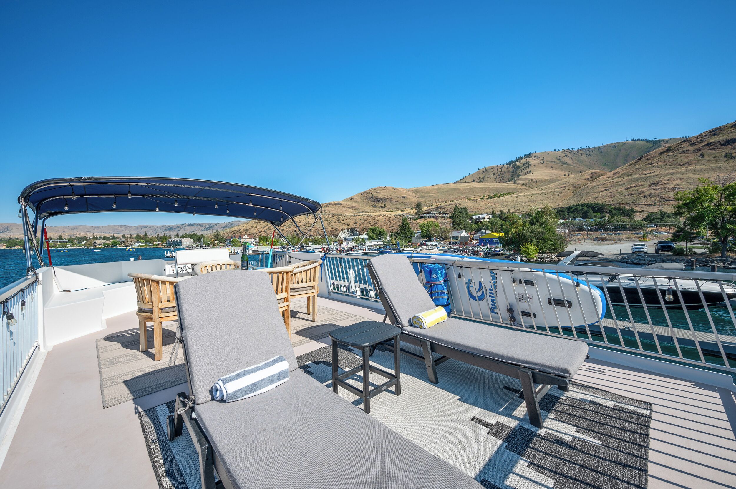 A deck with lounge chairs, a table, and a covered area overlooking a body of water and hills.
