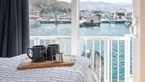 Un letto con vista su un porto turistico e barche, un vassoio di legno con tazze e una ringhiera bianca.