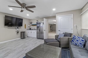 Una sala de estar moderna con una televisión de pantalla plana, ventilador de techo y una zona de cocina con refrigerador y microondas.
