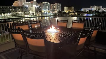 A round table with chairs on a balcony overlooking a cityscape at night.