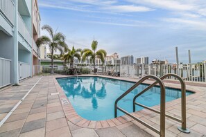 A swimming pool with a metal ladder, surrounded by a tiled deck and palm trees.