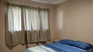 A bedroom with a bed, curtains, and a nightstand.