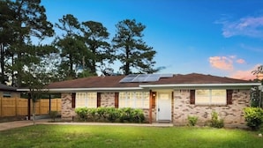 A single-story brick house with a front door, windows, and solar panels on the roof.