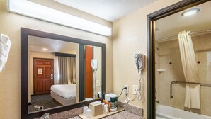 Une salle de bain d’hôtel équipée d’un lavabo, d’un miroir, d’un sèche-cheveux et d’une douche.
