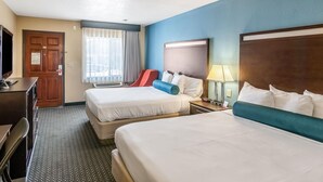 Habitación de hotel con dos camas, un escritorio, un televisor y una ventana con cortinas.