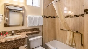 Un baño con lavamanos de encimera de granito, espejo, toallero, ducha con cortina y retrete.