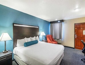 A hotel room with a large bed, two bedside lamps, a red chair, a wooden door, and a window with curtains. - NK-King Non-Smoking. (Glendale)