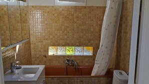 Ein Badezimmer mit Badewanne, Toilette und Waschbecken. Über der Badewanne befindet sich ein Fenster und ein Duschvorhang.
