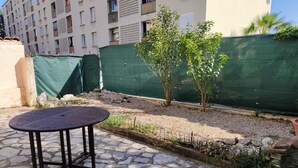 Eine Terrasse mit einem runden Tisch, einem grünen Zaun und einem kleinen Baum.