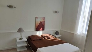 Ein Schlafzimmer mit Bett, Nachttisch, Lampe, Wandbild und Fenster.