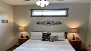 Une chambre avec un grand lit, deux tables de chevet avec des lampes, un élément décoratif mural au-dessus du lit et une fenêtre laissant entrer la lumière naturelle.