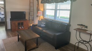 A living room with a black leather sofa, a wooden coffee table, a television on a wooden cabinet, a ladder, and a window with blinds. - Sleeps 5 (unit 4b), pool, next to Big M Marina, 15 min to Roaring River (Cassville)