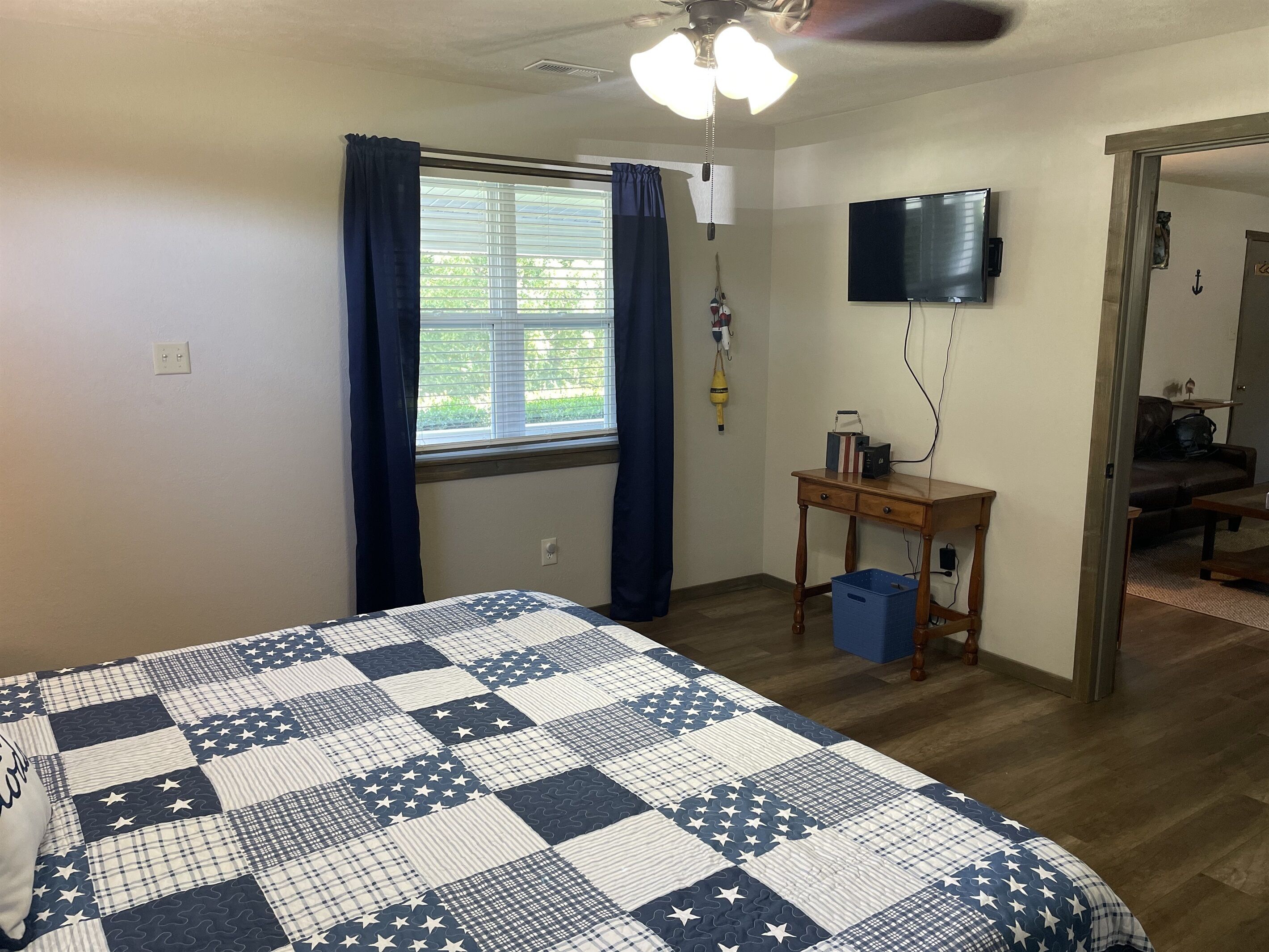 A bedroom with a bed, a desk, a television, and a ceiling fan.