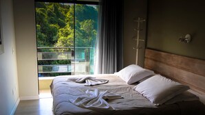 A bedroom with a large window, a wooden headboard, and a neatly made bed with white linens. - Pousada Porto do Arvoredo (Florianópolis)