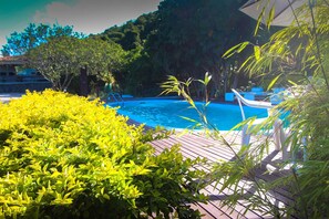 A pool area with a wooden deck, surrounded by lush greenery and a clear blue pool. - Pousada Porto do Arvoredo (Florianópolis)