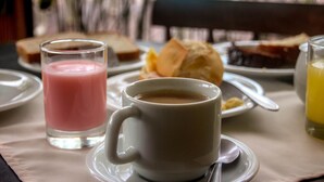 A breakfast setting with a cup of coffee, a glass of pink smoothie, and a plate with toast and a pastry. - Pousada Porto do Arvoredo (Florianópolis)