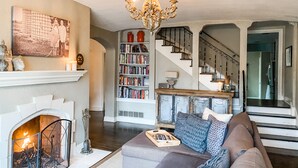 A living room with a fireplace, bookshelves, a chandelier, and a staircase. - Spacious Historic Midtown Memphis Chateau Minutes from Everything  (Memphis)