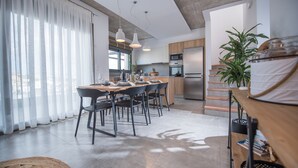 A modern kitchen with a dining area, featuring a large window, wooden cabinets, and a built-in oven. - Emmeleia mare new building maisonette with pool, seaview, 3 min from the beach  (Αγία Πελαγία)