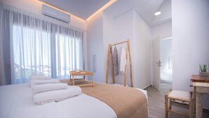 A modern hotel room with a large bed, a wooden chair, a desk, and a view of the city through the window. - Emmeleia mare new building maisonette with pool, seaview, 3 min from the beach  (Αγία Πελαγία)