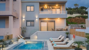 Um edifício moderno com piscina, espreguiçadeiras e varanda com assentos.