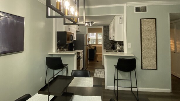 A modern kitchen with white cabinets, a black countertop, and a built-in microwave. There is a dining area with a table and chairs, and a black chair is visible. - Newly Renovated Cozy/Modern Pet-Friendly Villa for the entire family to enjoy. (Hilton Head Island)