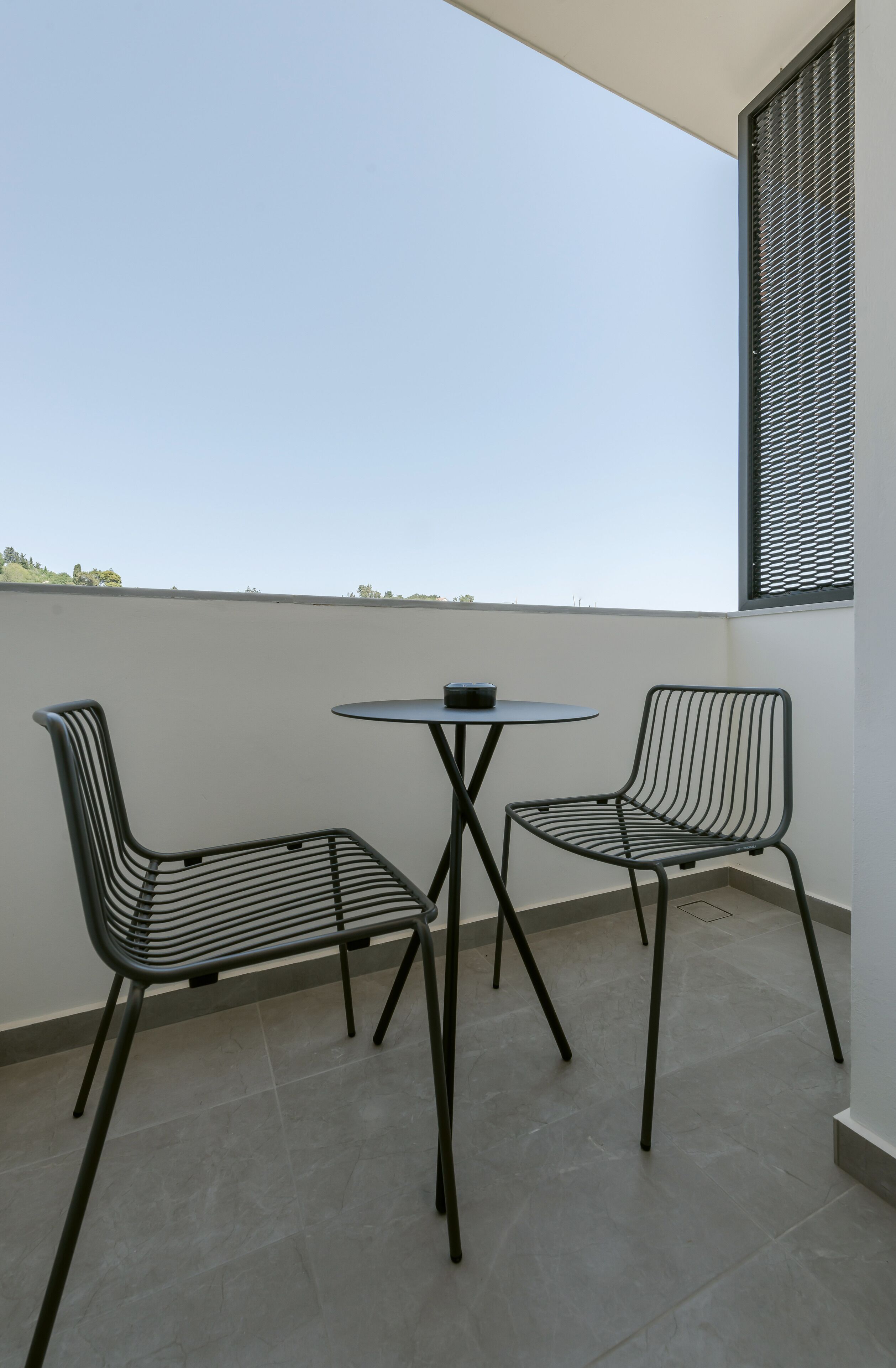 A balcony with two metal chairs and a small round table.