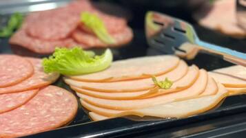 A buffet with sliced meats, including ham and salami, and a bowl of olives.