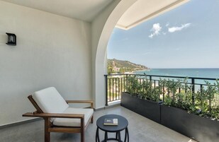 Un balcone con una sedia bianca, un tavolino rotondo e vista sul mare.