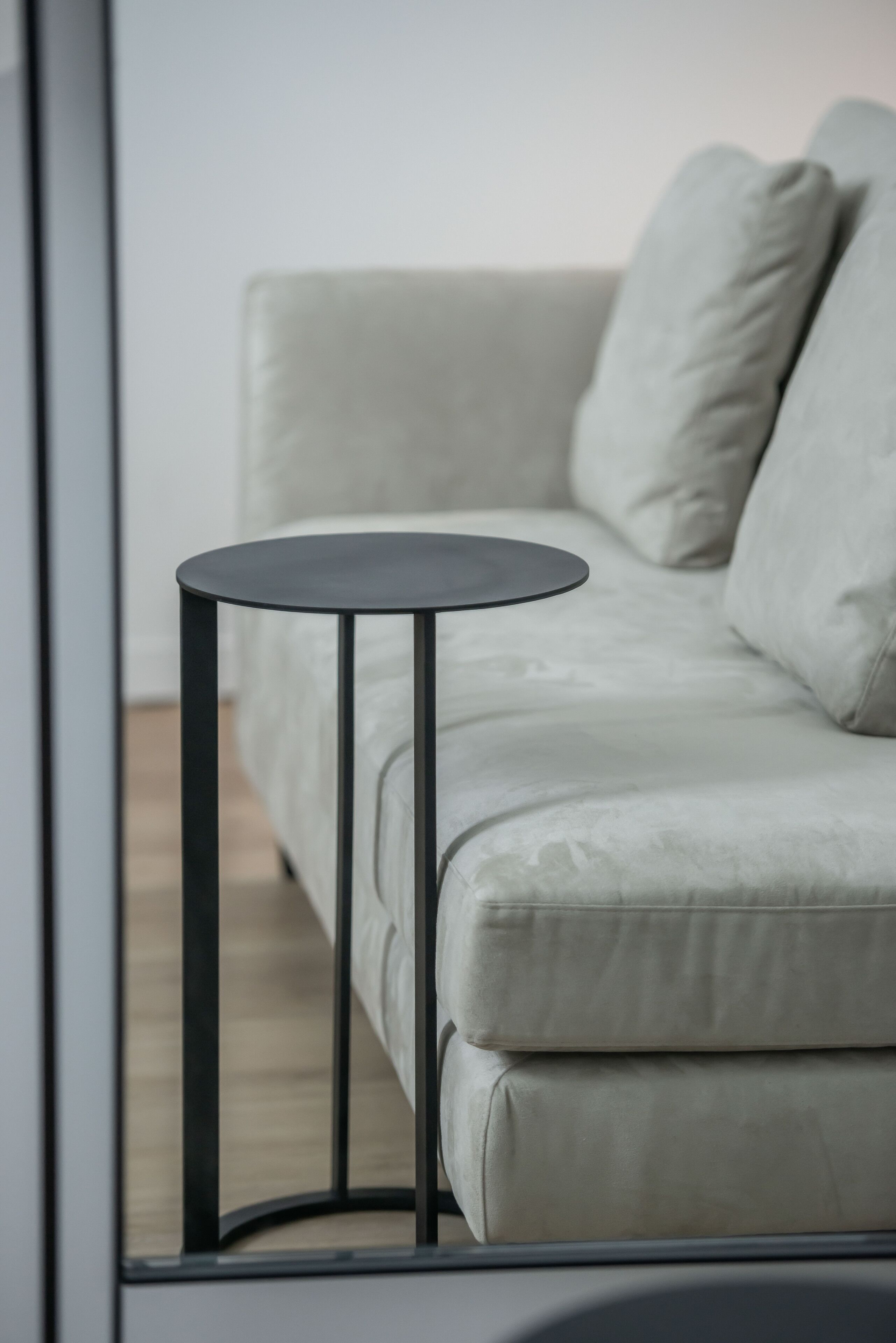 A modern living room with a light-colored sofa, a round black side table, and a visible wooden floor.