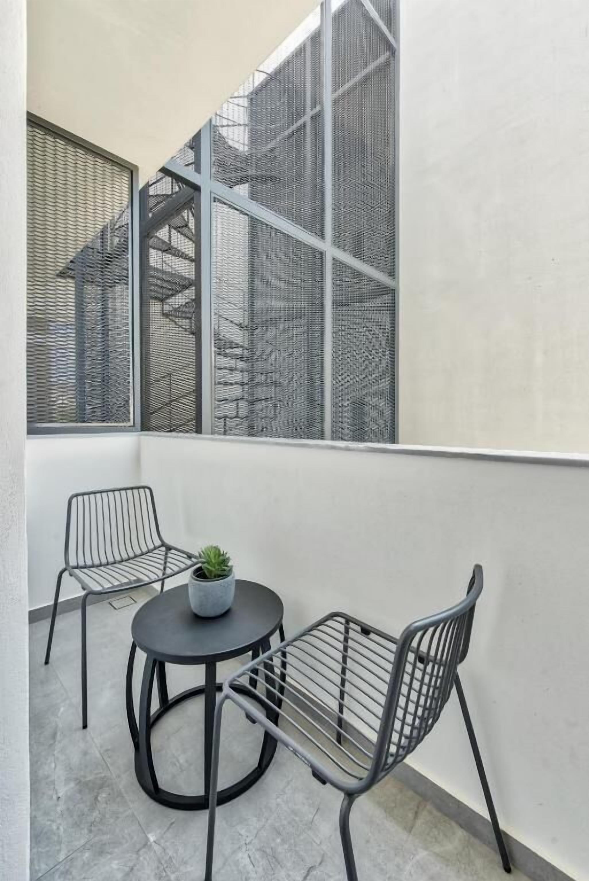 A small balcony with two metal chairs and a round table, featuring a potted plant.