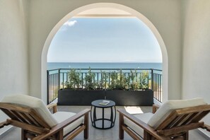 A balcony with two wooden lounge chairs, a small round table, and a view of the sea. - Bitzaro Boutique Hotel (Zakynthos)