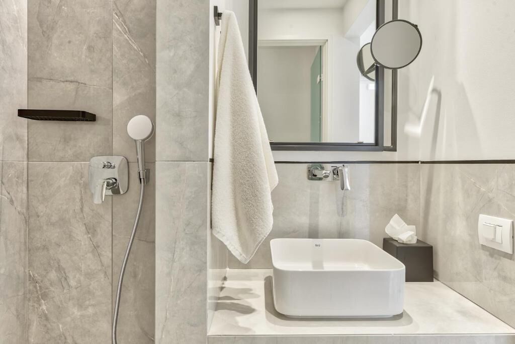 Un baño moderno con un lavabo blanco, una toalla colgada en un perchero, un espejo y un dispensador de toallas.