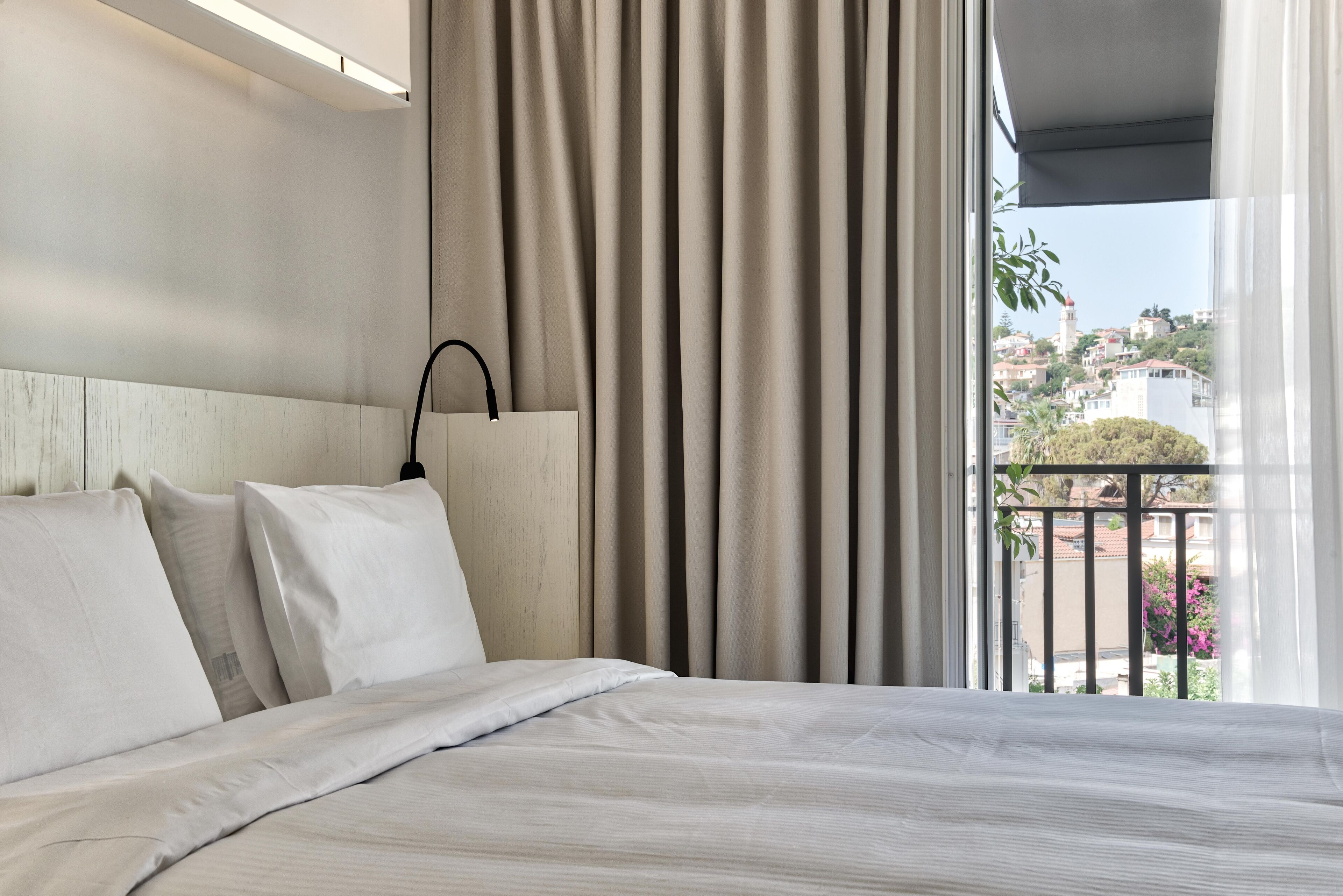 Une chambre d’hôtel avec un lit, des rideaux, une tête de lit et une vue sur la ville par une fenêtre.