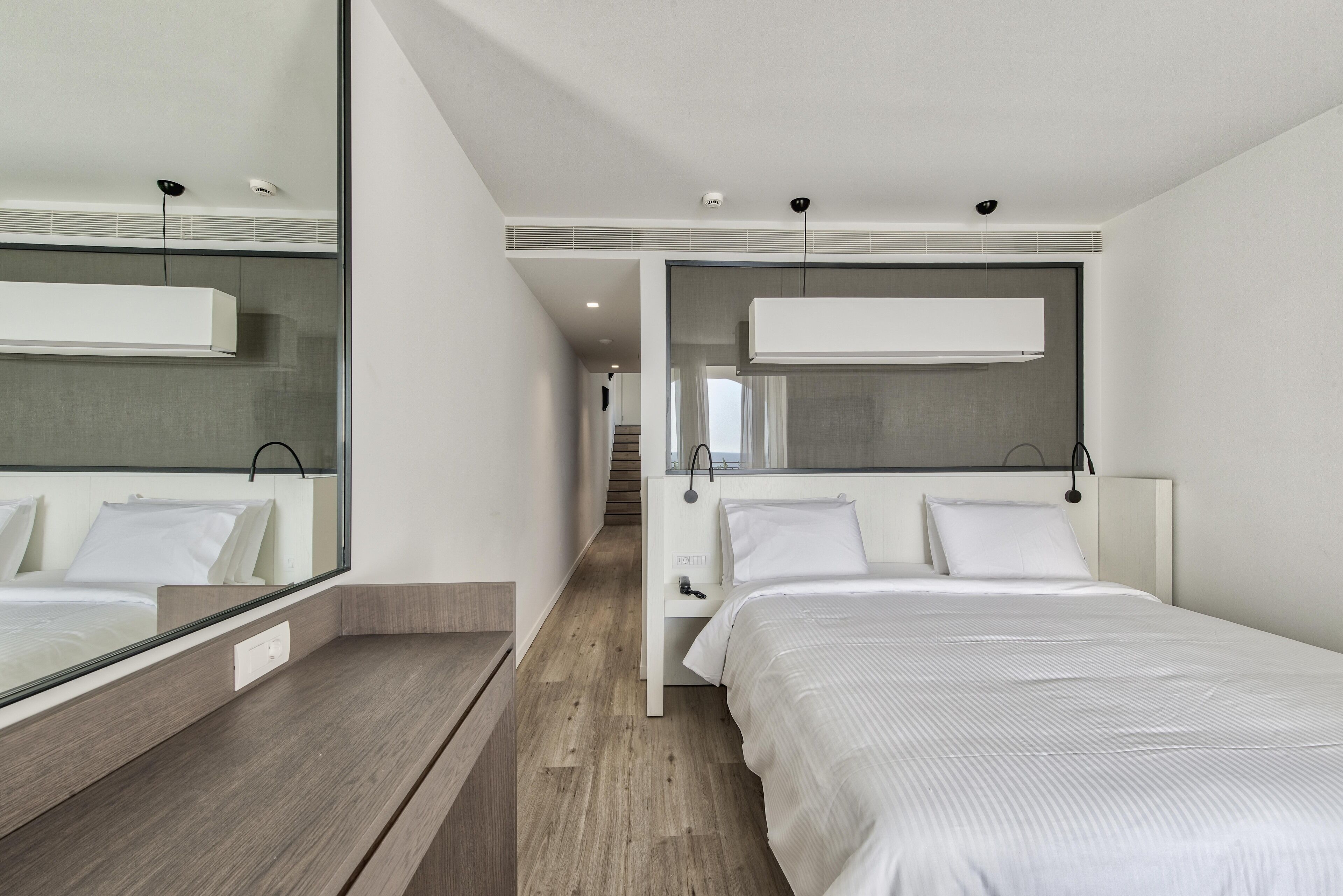 A modern hotel room with a large bed, a bedside table, a mirror, and a view of the hallway.