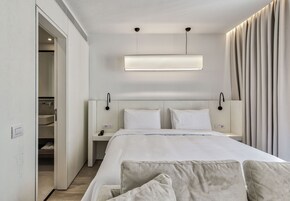 A modern hotel room with a large bed, bedside tables, a wardrobe, and a ceiling-mounted light fixture.