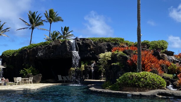 Ein Poolbereich mit Wasserfall, Palmen und Liegestühlen.