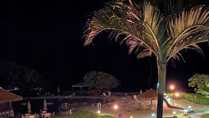 Ein Nachtblick auf eine angelegte Grünfläche mit Pool, Palmen und Außenmöbeln.