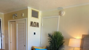 Ein Hotelzimmer mit Bett, Sessel, Pflanze und Wand mit Lüftung und Hinweisschild.