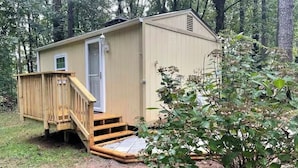 A small, single-story wooden shed with a door and a small window, surrounded by a wooden deck and steps leading up to it. - Tiny House Near Stone Mountain Park Minutes to Atlanta and FIFA.  (Lilburn)