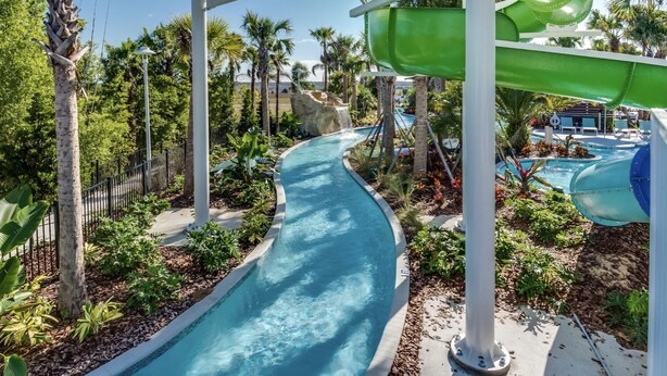 A water slide with a pool at the bottom, surrounded by palm trees and a poolside area with lounge chairs.