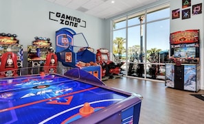 A gaming area with a pool table, various arcade games, and a large window offering a view of palm trees.