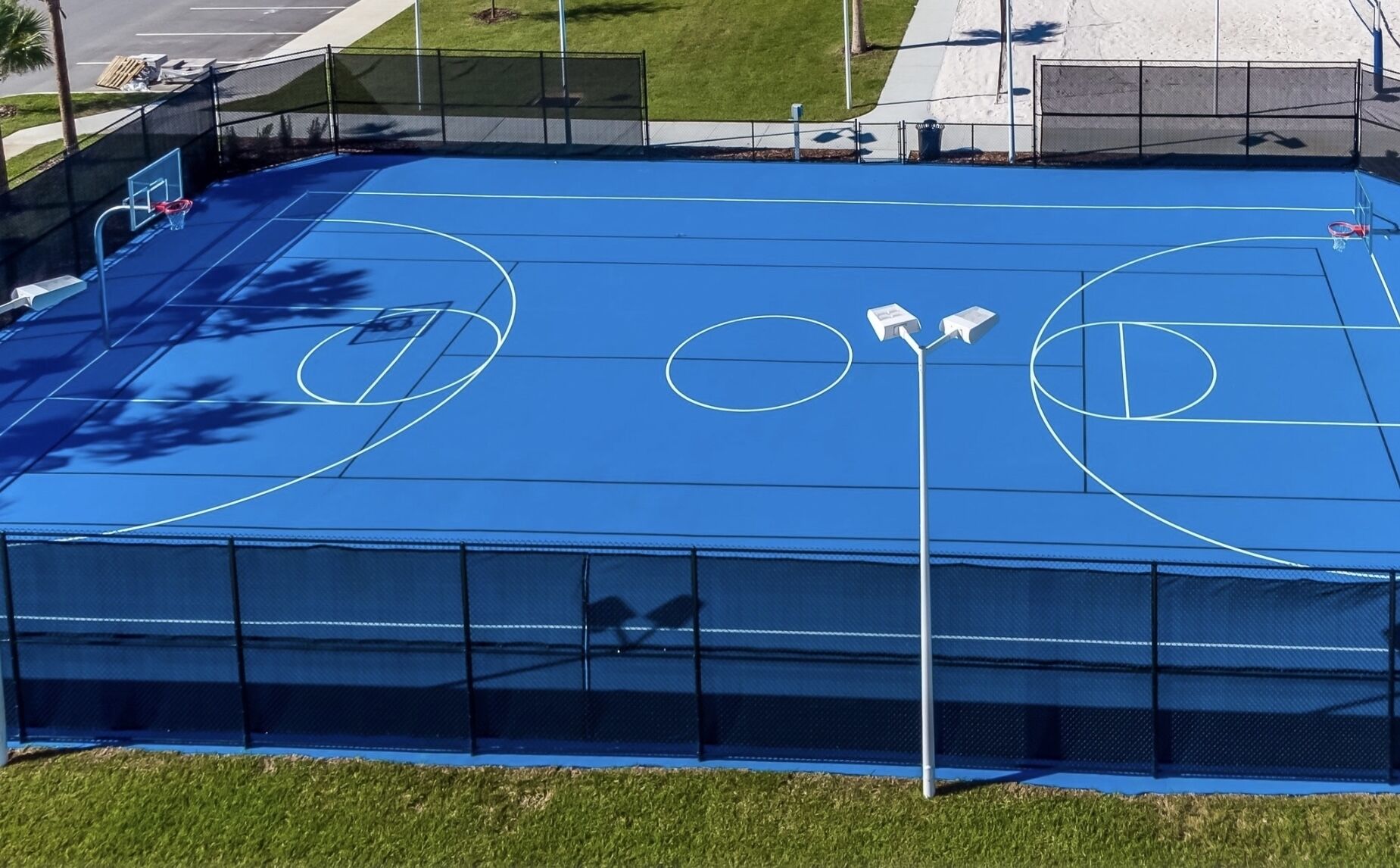 Una cancha de baloncesto al aire libre con superficie azul, rodeada por una valla.