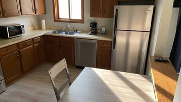 Une cuisine avec des meubles de rangement en bois, un réfrigérateur en acier inoxydable, un lave-vaisselle, un four à micro-ondes, une fenêtre et une table avec des chaises.