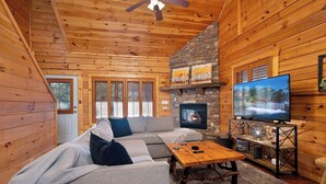 L’intérieur d’une cabane en rondins, avec une cheminée en pierre, un téléviseur, un canapé et une table basse en bois.
